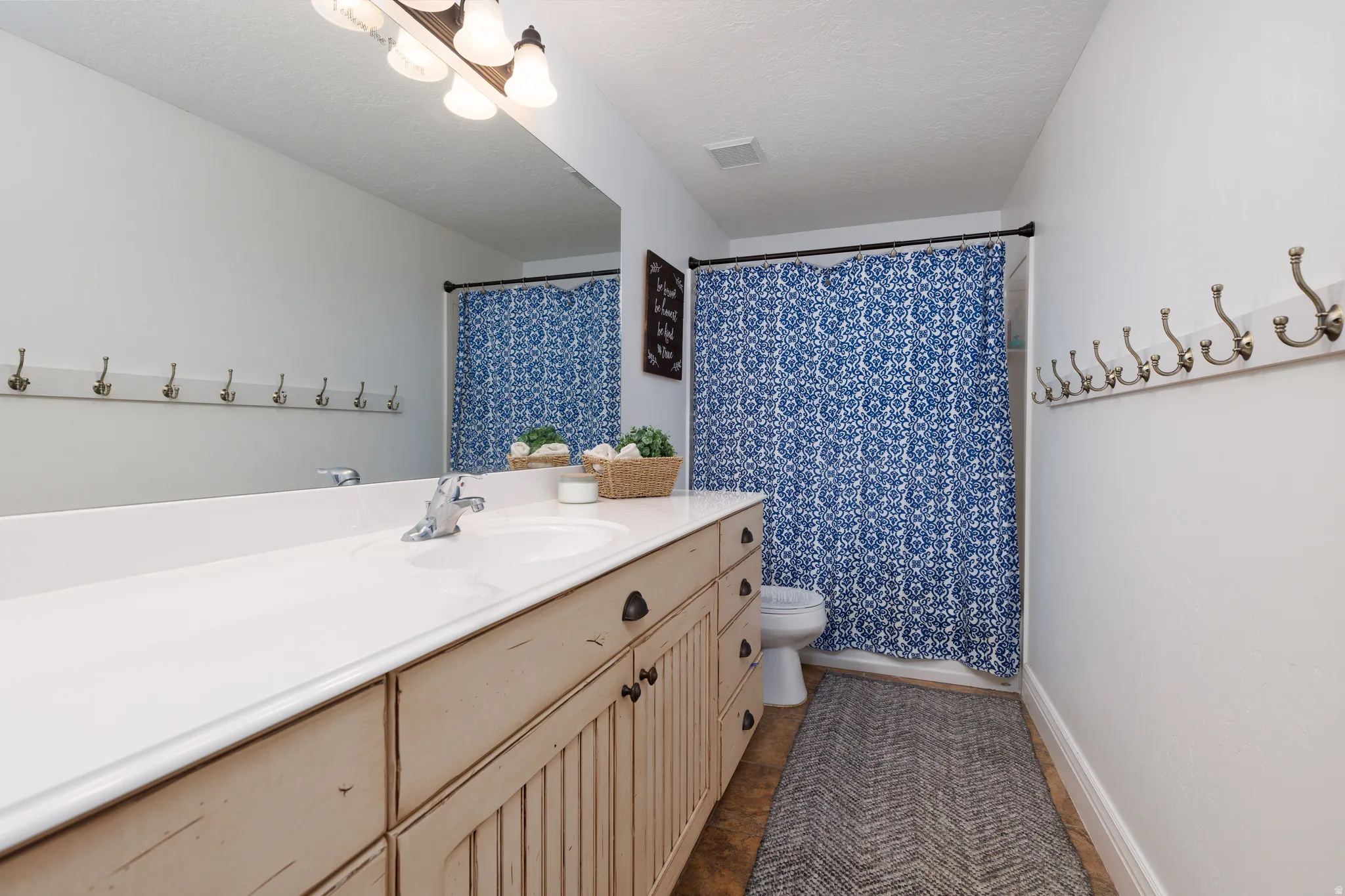 Bathroom featuring an extended single-sink vanity with distressed wood-finish cabinetry, a full-width mirror, and a wall-mounted multi-hook rack