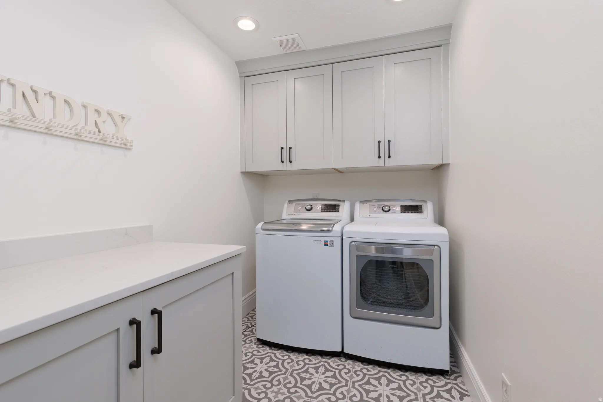 Dedicated laundry area featuring patterned floor tile, light gray cabinetry, and a white countertop