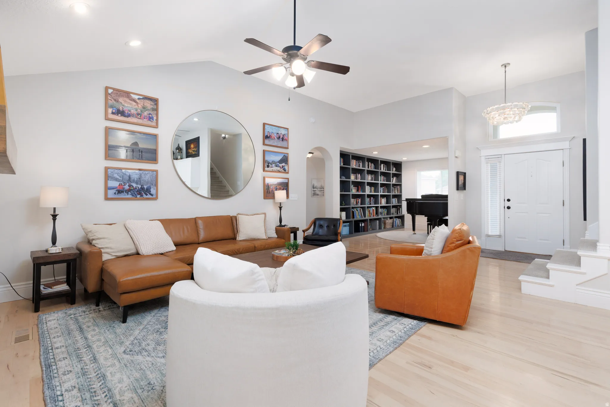 Spacious living area featuring light wood-finish flooring, vaulted ceilings, and a ceiling fan