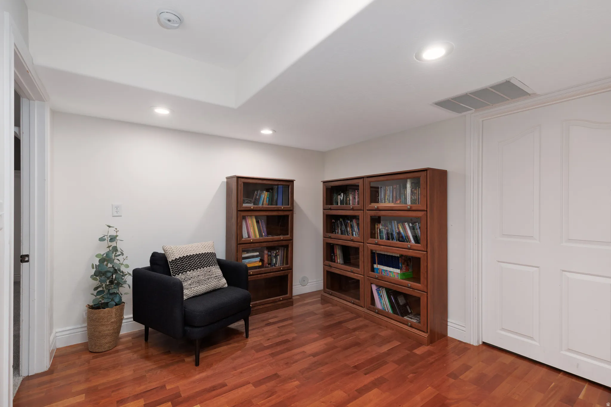 Recessed lighting illuminates a space featuring wood-finish flooring