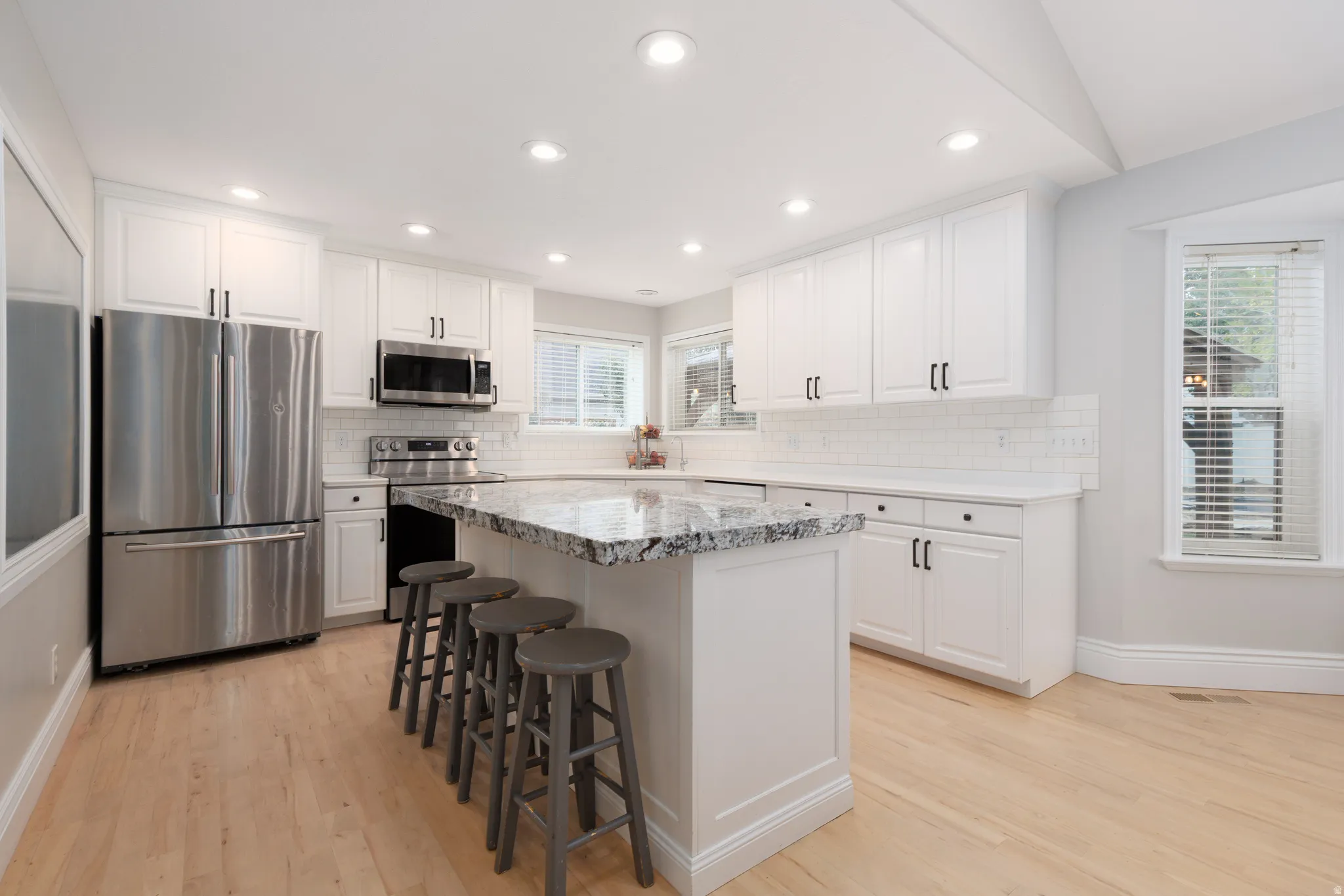 Bright kitchen with light wood-finish flooring, white cabinetry, and recessed lighting