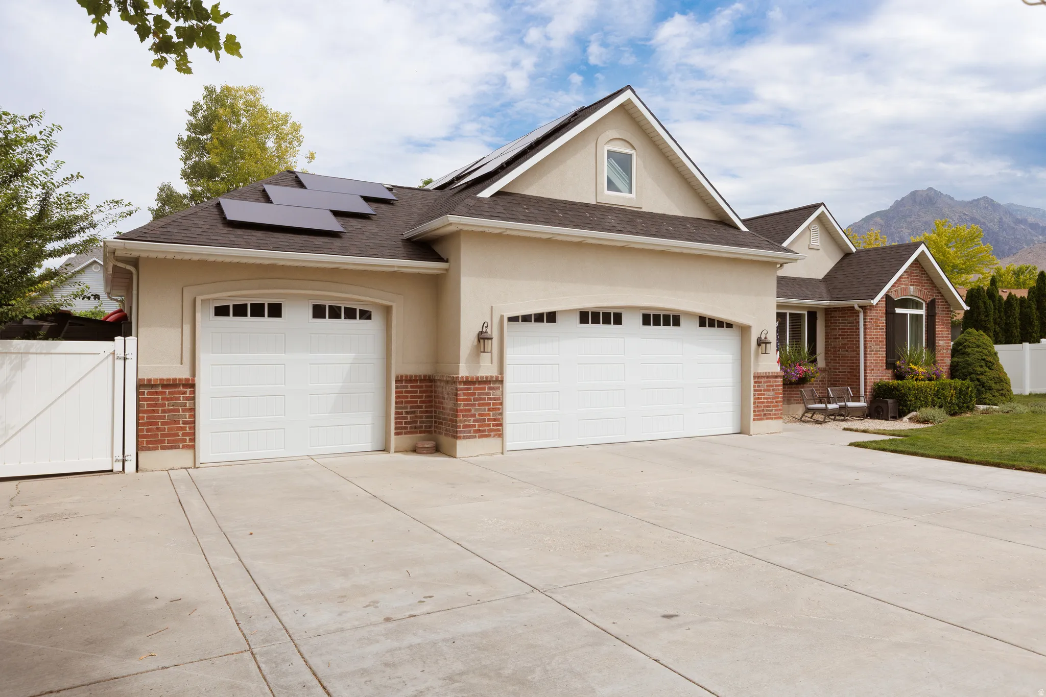 Stucco and brick exterior featuring a two-car garage, an additional one-car garage, solar panels, and a mountain backdrop
