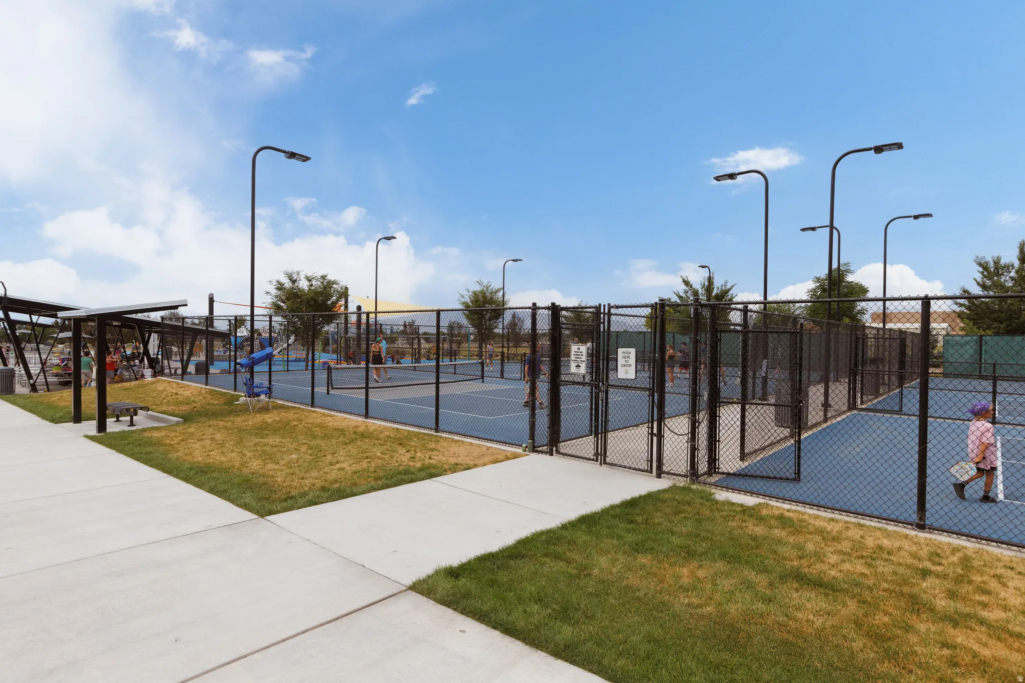 Recreational court area featuring multiple blue-surfaced courts, perimeter chain-link fencing, and overhead lighting fixtures