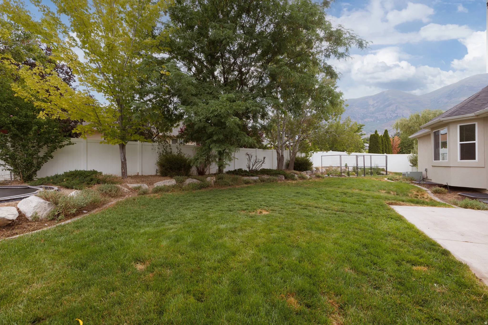 Expansive backyard featuring a lush lawn, mature trees, white privacy fencing, and mountain backdrop