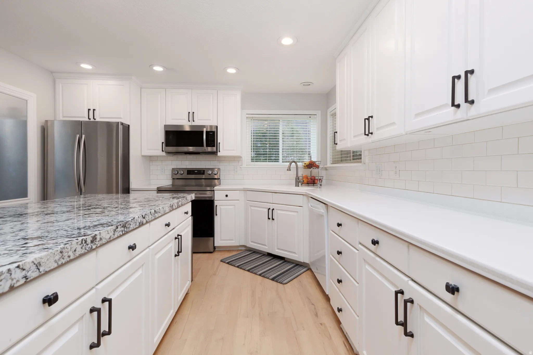 Bright kitchen featuring white cabinetry, light wood-finish flooring, recessed lighting, and stainless steel appliances