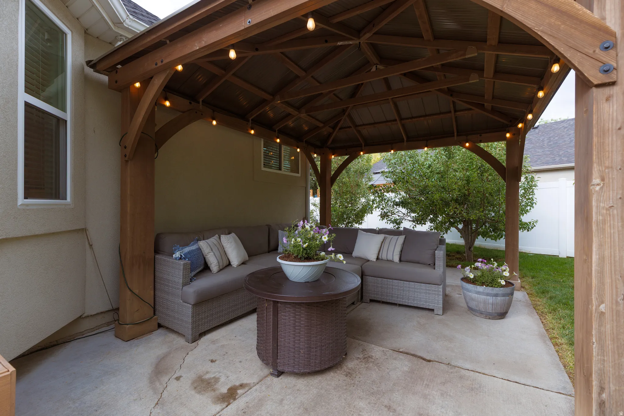 Covered outdoor patio featuring a wood-frame gazebo with string lighting and a corrugated metal roof