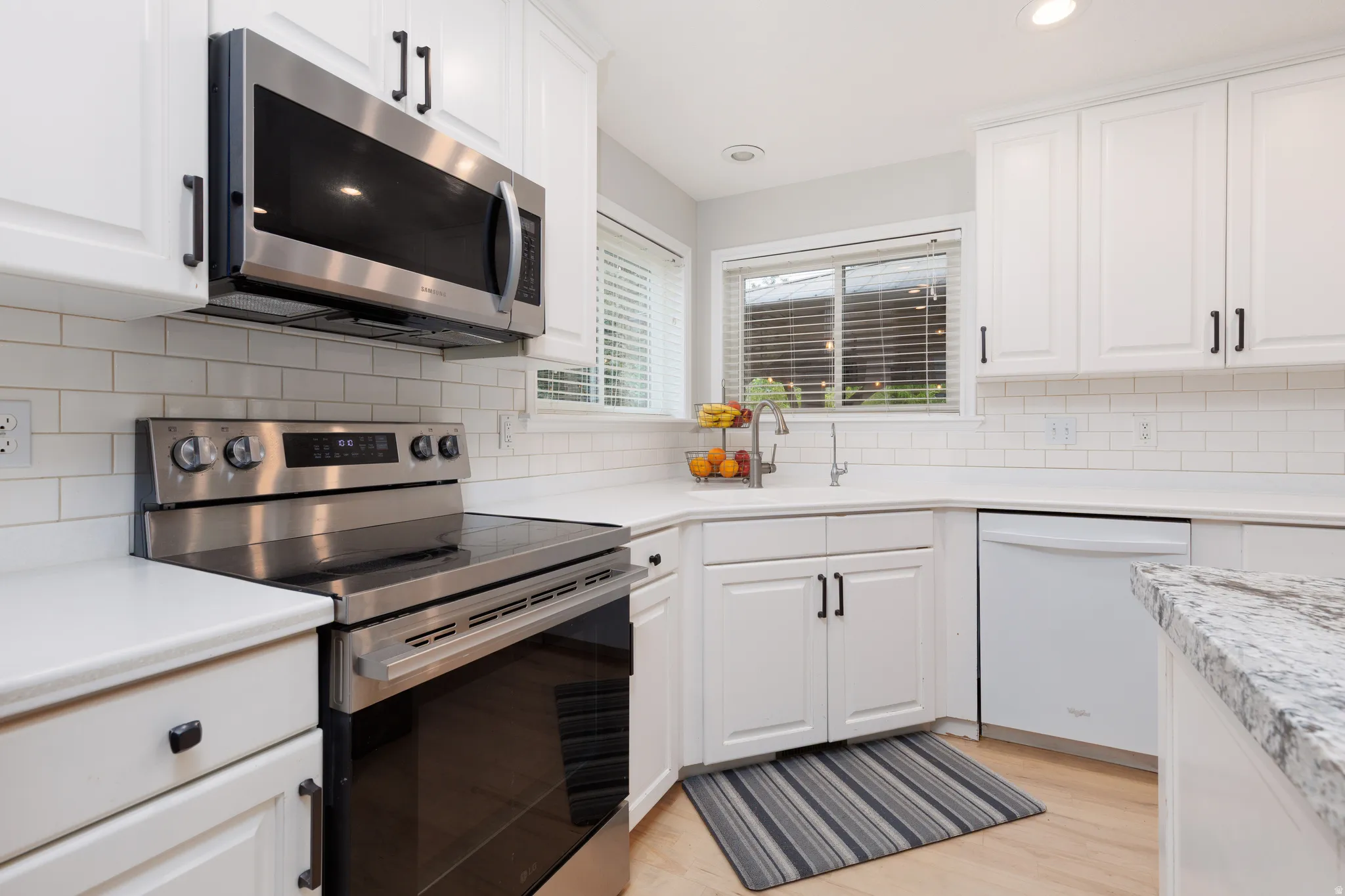 Kitchen featuring white cabinetry with dark hardware, stainless steel appliances, a white subway tile backsplash, and light wood-finish flooring