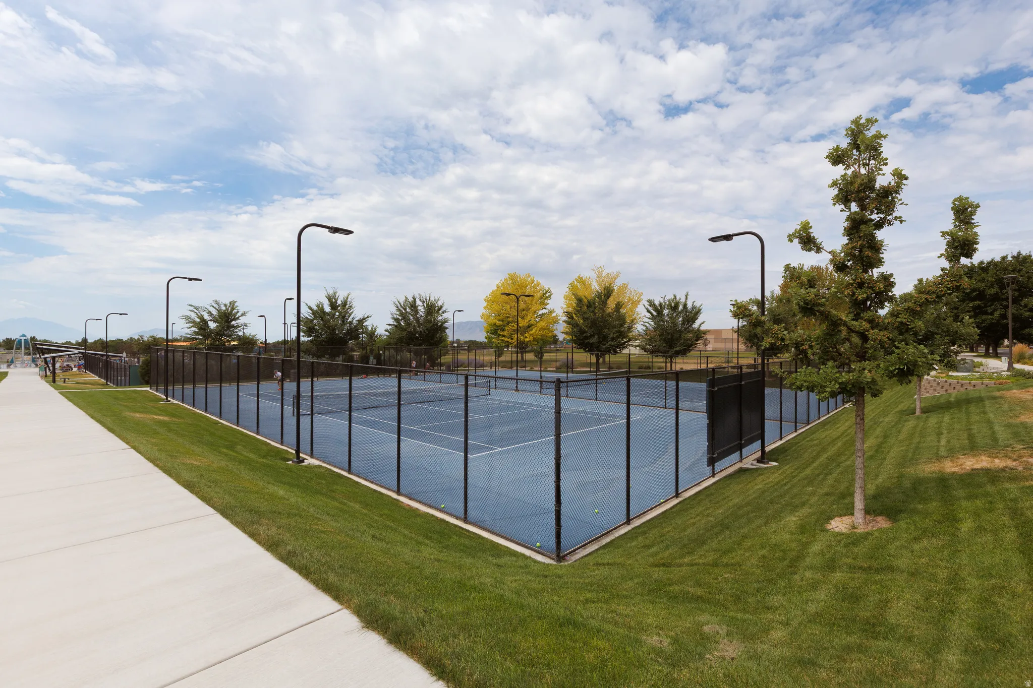 Outdoor tennis courts featuring a blue playing surface, black perimeter fencing, and integrated lighting