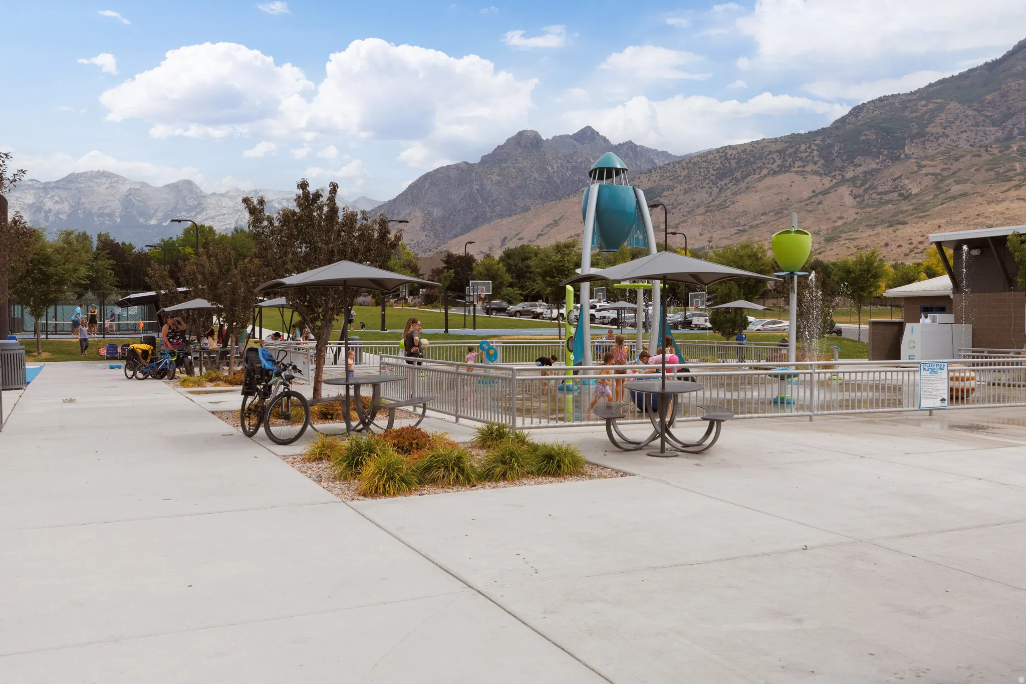 Integrated splash pad area featuring modern water features, surrounding concrete pathways, and multiple shaded picnic tables