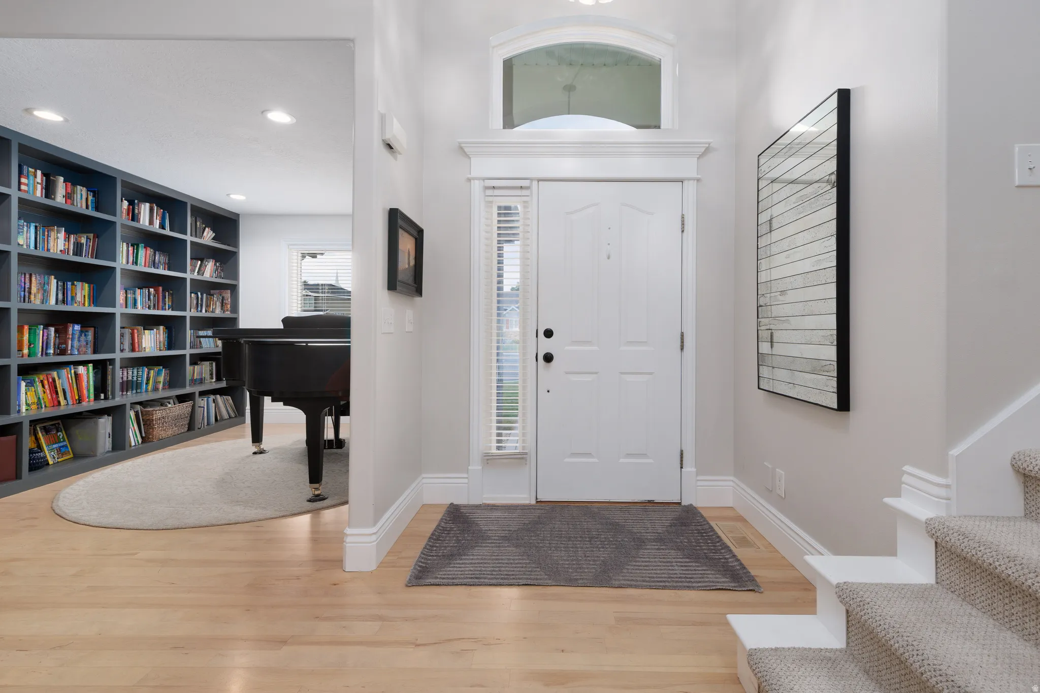 Entryway with light wood-finish flooring, a white paneled door with an arched transom, and a carpeted staircase
