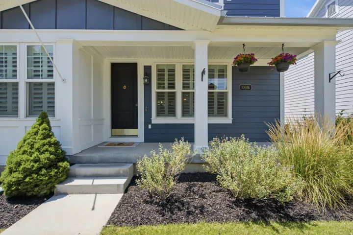 Covered front porch with white columns, concrete steps, and a dark blue entry door