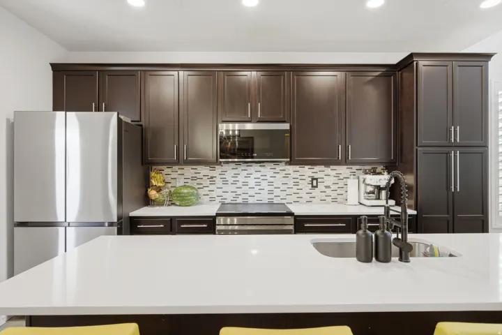Kitchen featuring dark wood cabinetry with crown molding, a stainless steel French door refrigerator, white countertops, and a mosaic tile backsplash