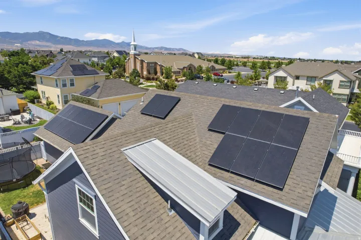 Multiple solar panels installed on the shingle roofing of a two-story residence with blue siding