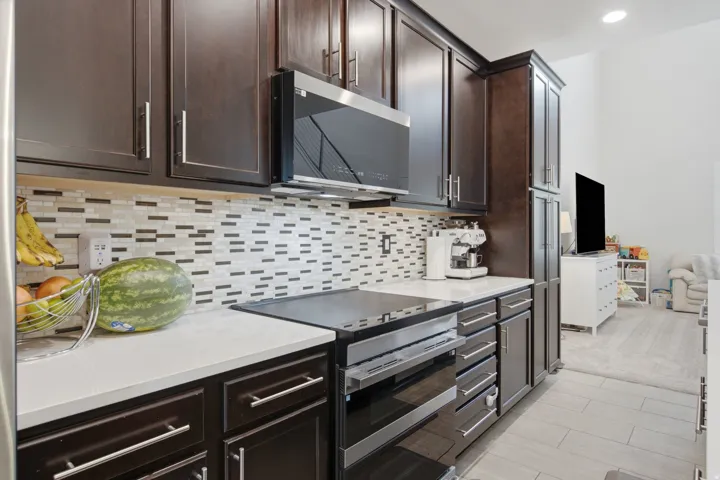 Kitchen featuring dark wood cabinetry, white countertops, tile backsplash, built-in microwave, and electric range with oven