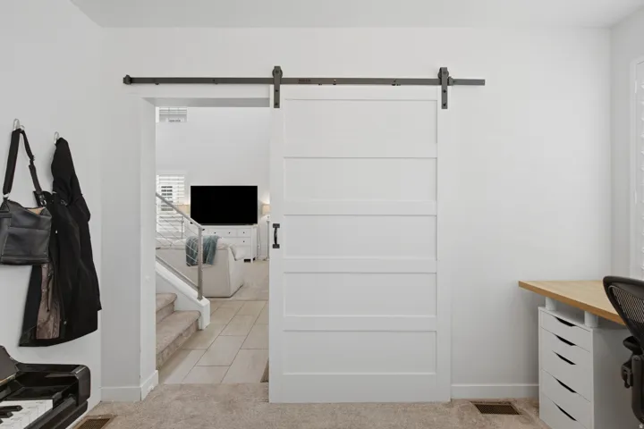White four-panel barn door on a black metal track, opening to reveal interior spaces