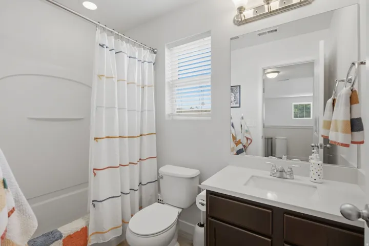 Bathroom featuring a built-in tub with shower, a brown wood-finish vanity with an integrated sink, a rectangular mirror, and a window with blinds
