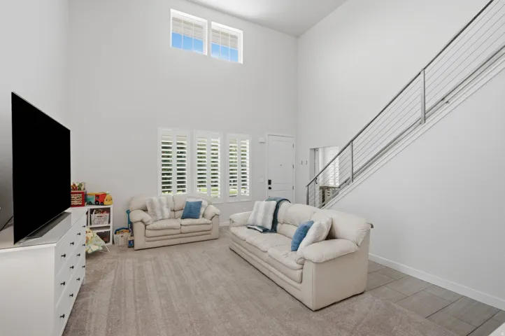 Vaulted ceiling living area featuring upper transom windows and three large windows with plantation shutters