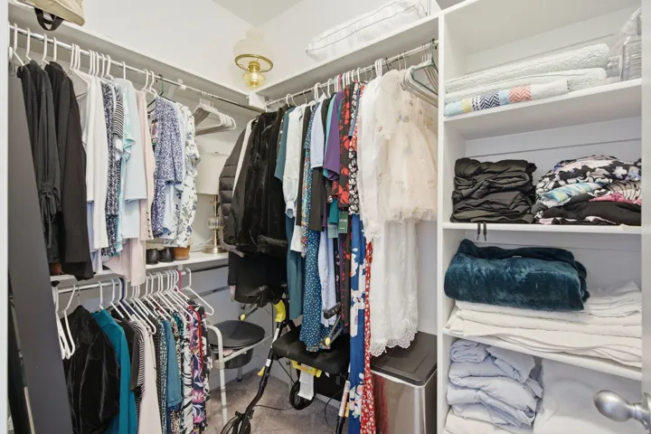 Walk-in closet featuring white shelving, multiple hanging rods, built-in organizers, and overhead lighting