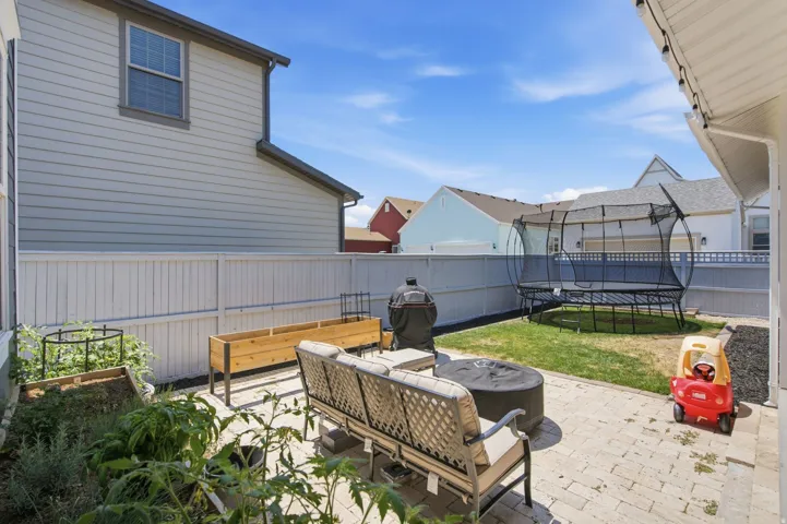 Expansive backyard featuring a white privacy fence, paver patio, dedicated garden beds, and an artificial turf area