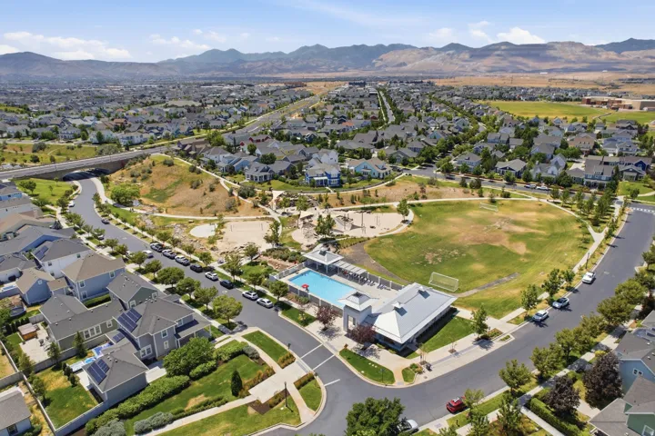 Aerial perspective of a planned community featuring residential properties, a large central park with green space and playground areas, and a community swimming pool with an adjacent building
