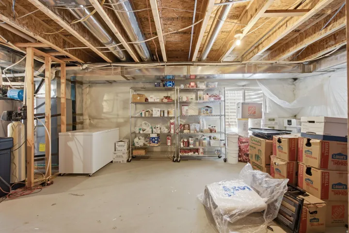 Unfinished basement with exposed ceiling joists and ductwork, concrete flooring, and a visible window opening