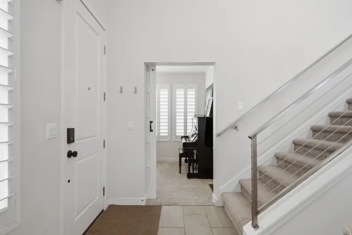 Entryway featuring a solid panel door with dark hardware, louvered window treatments, and tile flooring