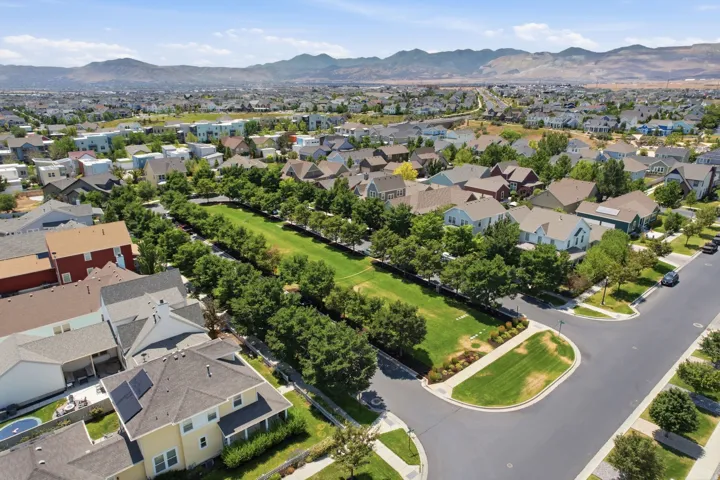Spacious neighborhood greenbelt with mature trees and paved streets, surrounded by residential properties with various architectural styles, including multi-story homes with solar panels