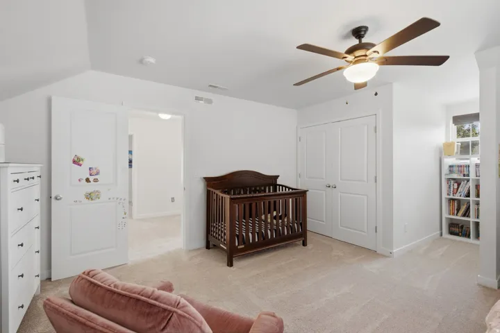 Spacious carpeted room featuring a ceiling fan with integrated lighting, double-door closet, and white built-in shelving