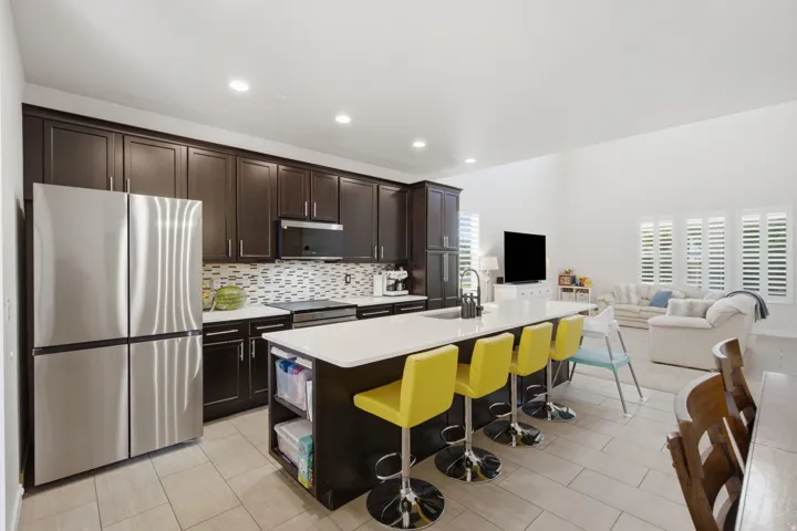 Modern kitchen featuring dark wood cabinetry, stainless steel appliances, a white tile backsplash, and a large island with a light-colored countertop