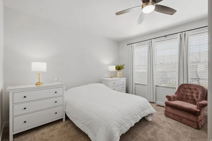 Spacious room featuring multiple windows with blinds and drapes, a ceiling fan with integrated lighting, and neutral-toned carpeting