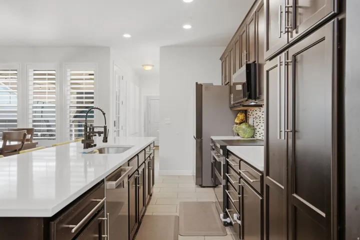 Kitchen featuring a large island with an undermount sink and matte black faucet, white countertops, dark wood-finish cabinetry, and stainless steel appliances