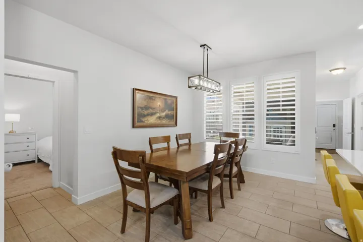 Dining area featuring a contemporary linear chandelier, three windows with plantation shutters, and tile flooring