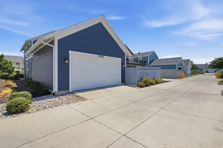 Detached residential building with blue and gray siding, featuring a white garage door, exterior wall lantern, and concrete driveway
