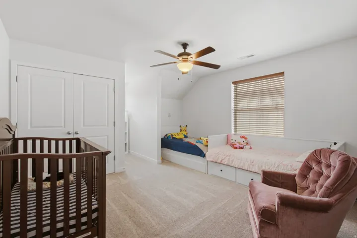 Carpeted room featuring a ceiling fan with light fixture, window with blinds, and white bi-fold closet doors