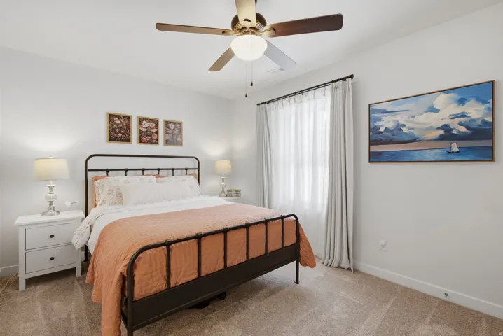 Carpeted room featuring a ceiling fan with integrated lighting, a window with sheer and blackout curtains, and light-toned walls