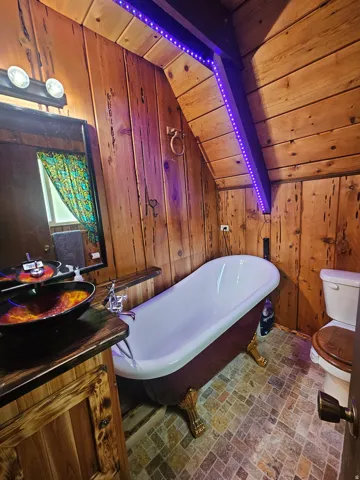 Full Bathroom on main featuring a freestanding clawfoot tub, wood-finish wall paneling, and a unique vessel sink on a wood vanity
