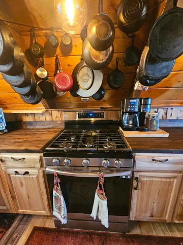 Stainless steel gas range with overhead wooden planking and hanging pot rack