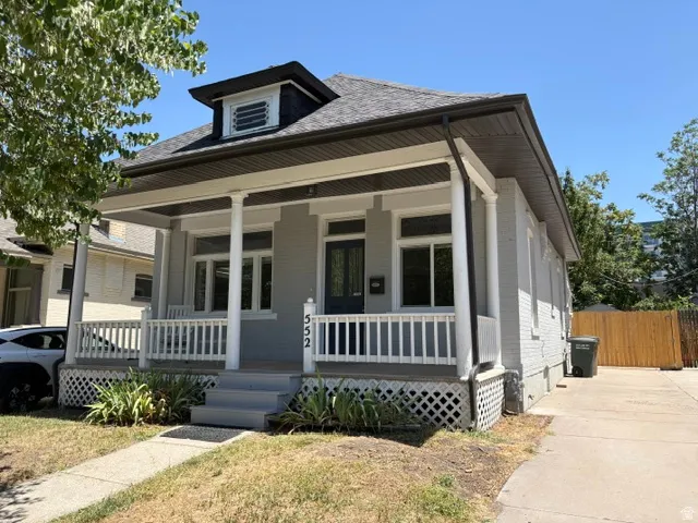 Gray painted brick exterior featuring a covered front porch with white columns, a dark gray roof, and a visible dormer