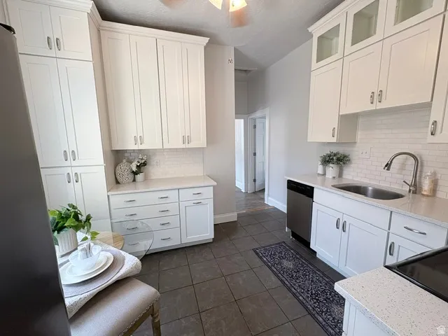 Modern kitchen featuring white shaker cabinetry, stainless steel dishwasher, white subway tile backsplash, light-toned countertops, and dark tile flooring