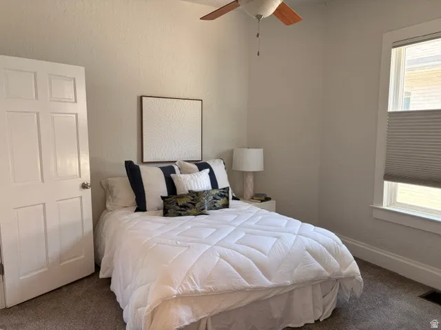 Neutral-toned room featuring a panel door, a window with cellular shades, a ceiling fan, and carpeted flooring