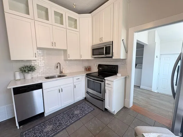 Contemporary kitchen featuring white cabinetry, subway tile backsplash, stainless steel appliances including a microwave, oven/range, and dishwasher, and light-toned countertops