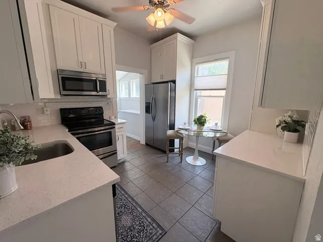 Kitchen featuring white cabinetry, stainless steel appliances, light-toned countertops, and a subway tile backsplash