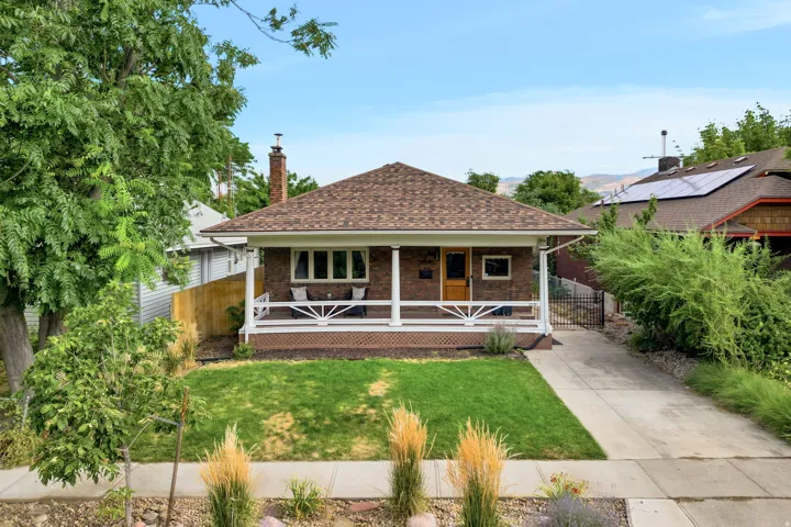 Brick facade home featuring a covered front porch with white railing, a dormer roof, and a mature front yard
