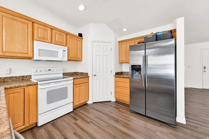 Kitchen featuring wood-finish cabinetry, white appliances, stainless steel refrigerator, and wood-finish flooring