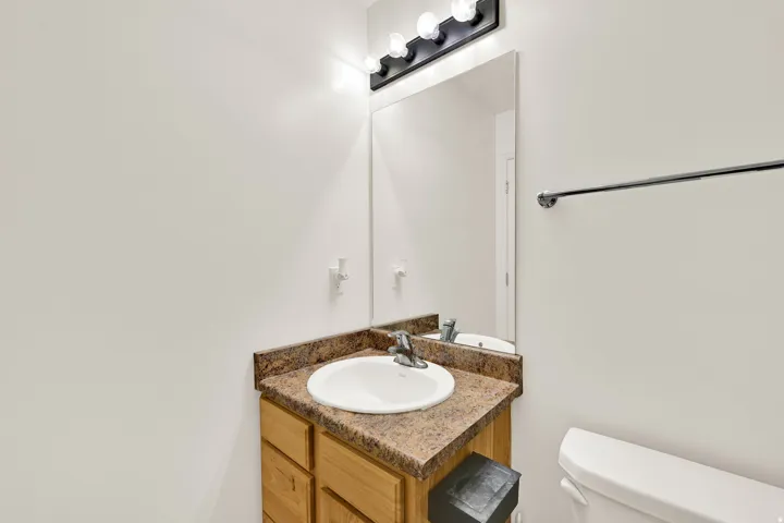 Bathroom vanity featuring a light wood-finish cabinet with storage, a speckled countertop, and an integrated white sink