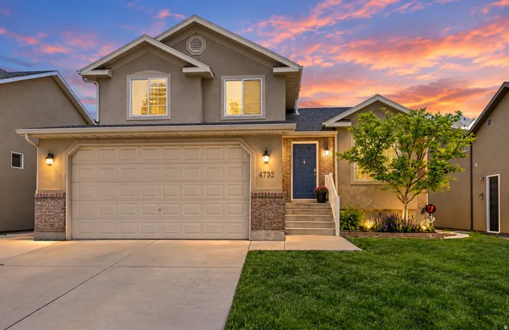 Stucco exterior with brick accents, attached two-car garage, concrete driveway, front entry with steps, and established landscaping