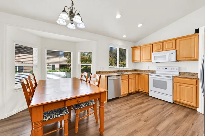 Kitchen featuring wood-finish flooring, light wood cabinetry, white appliances, and a bay window