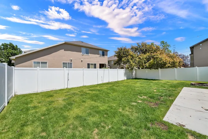 Spacious backyard featuring a manicured lawn, full privacy fencing, and a concrete patio area