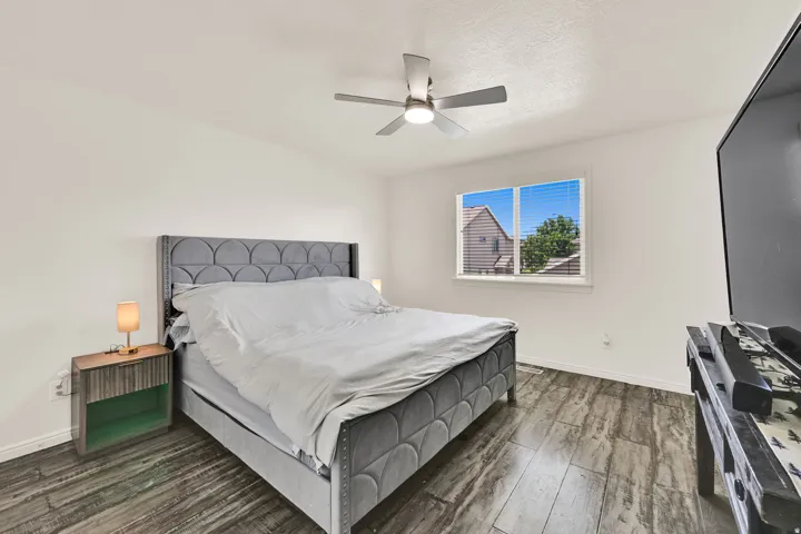 Bedroom featuring wood-finish flooring, white walls, and a ceiling fan with integrated lighting
