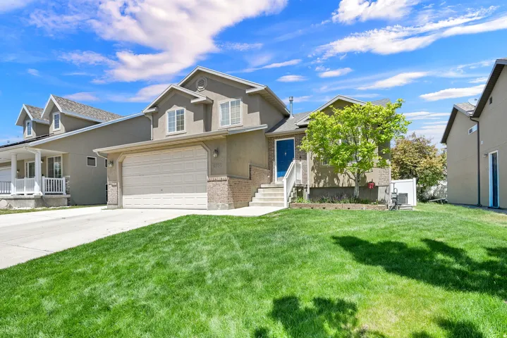 Stucco exterior home featuring a two-car garage, brick accents, and an established front lawn